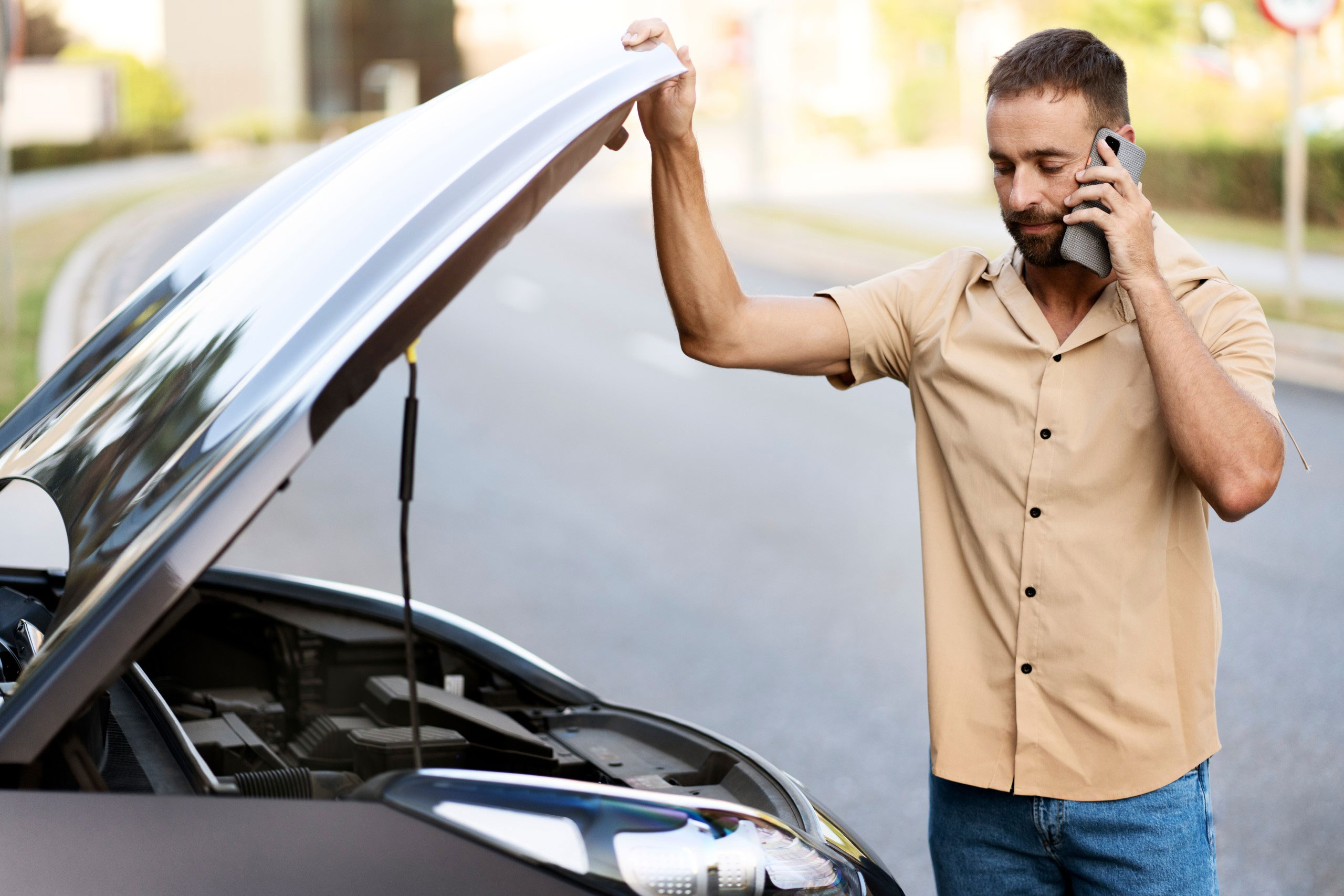 Man on the phone beside his broken-down car